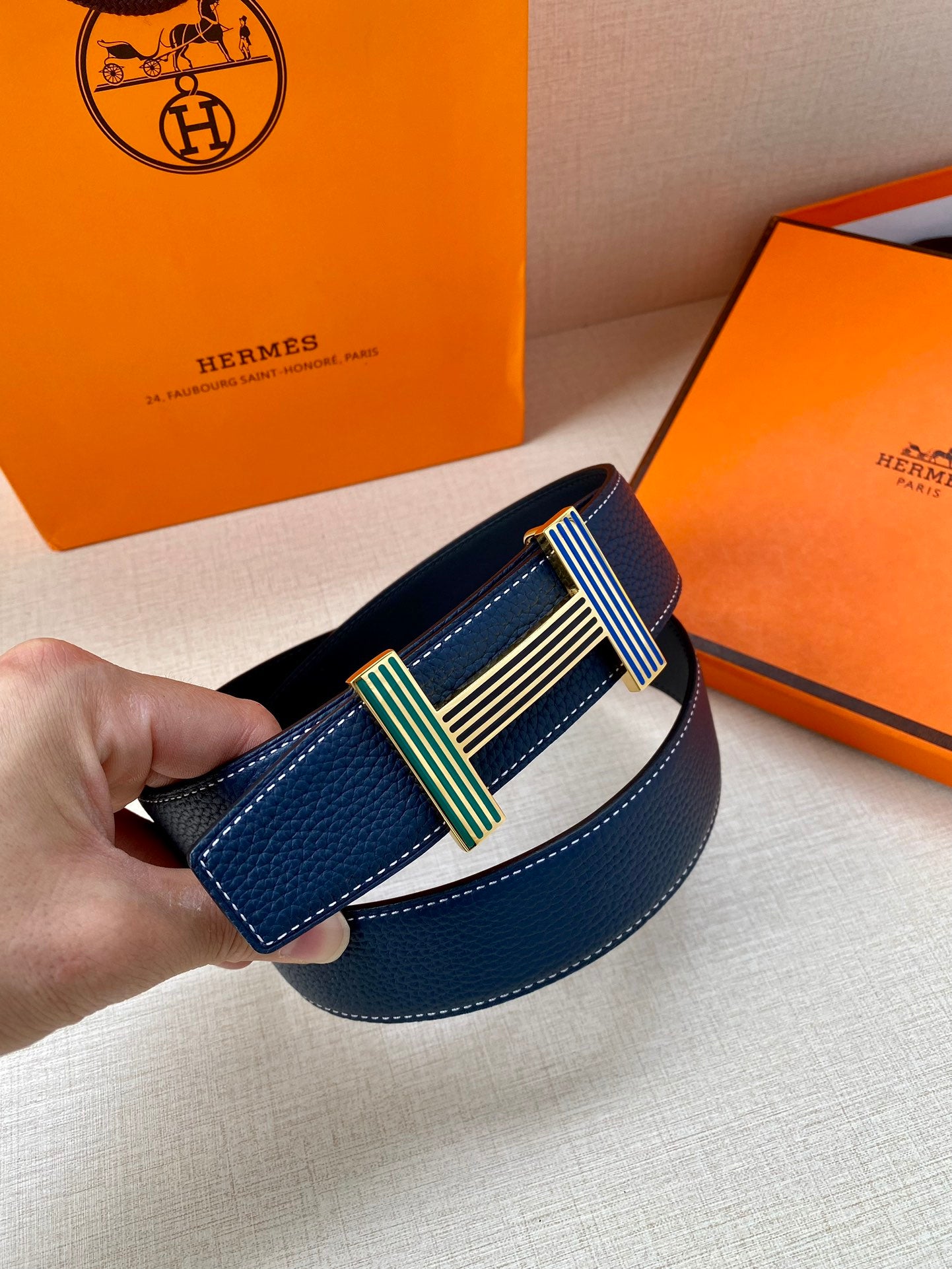 Blue leather belt with striped buckle, one end folded forward.