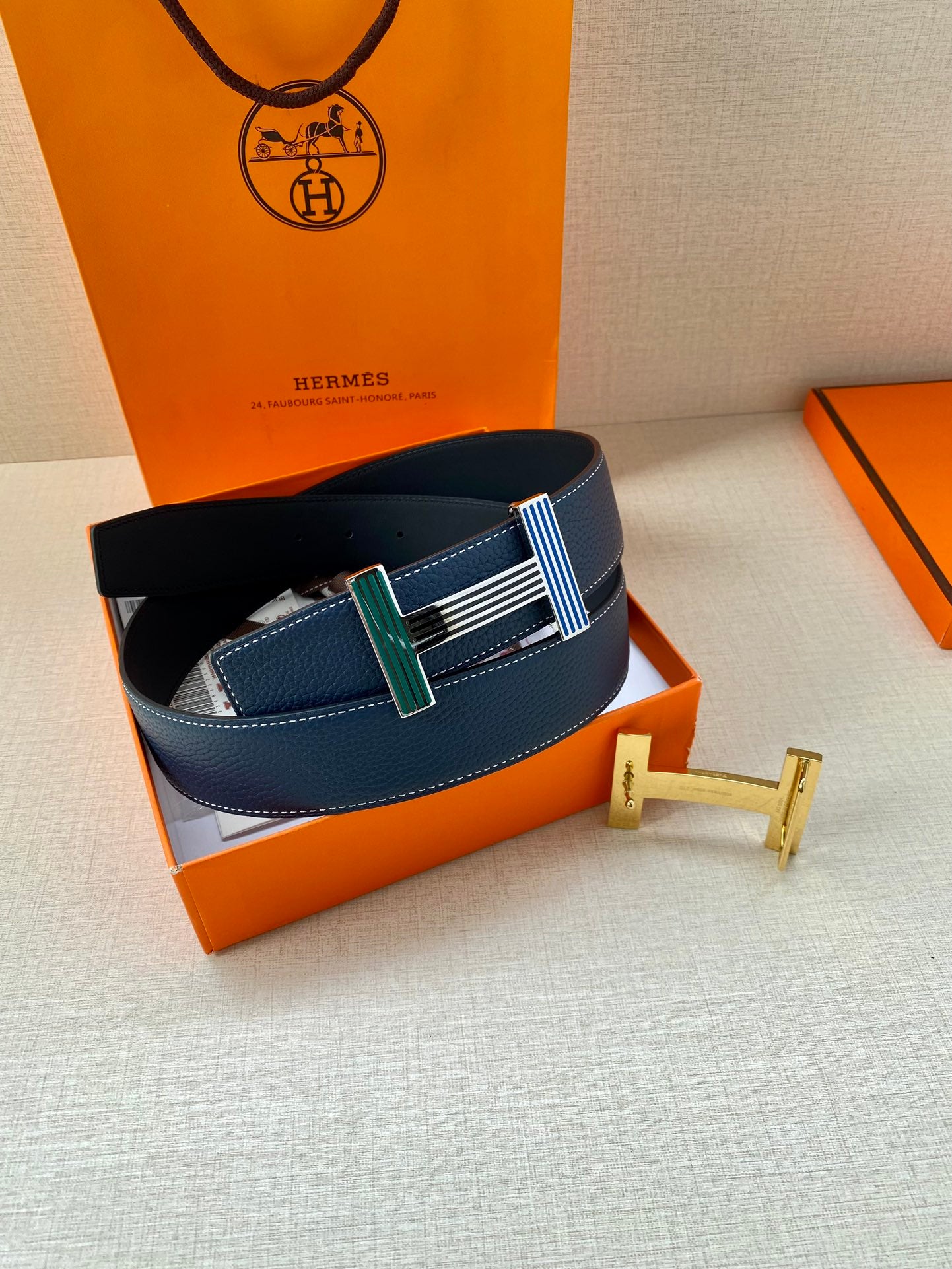 Blue leather belt in box with striped buckle and gold-toned H clasp