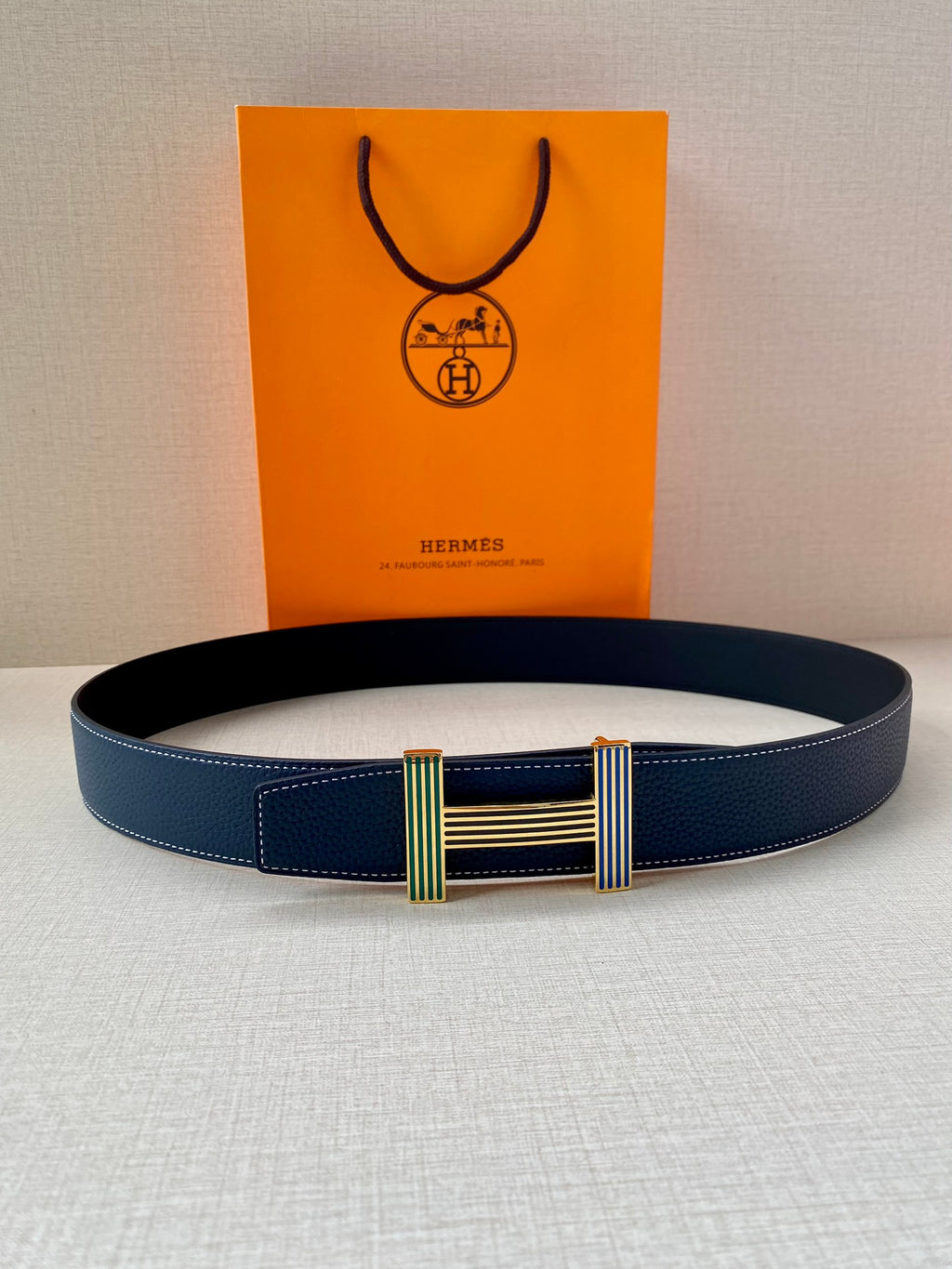 Blue leather belt with striped buckle and gold-tone bar accents, flat view.