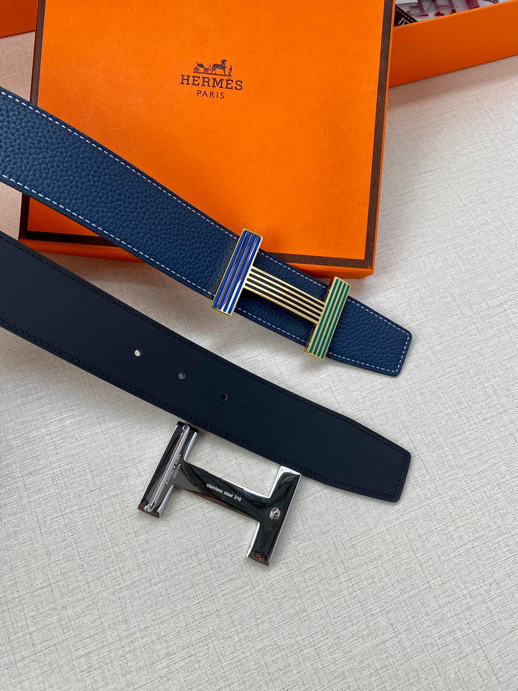 Blue leather belt with striped buckle; dark belt section lies underneath.