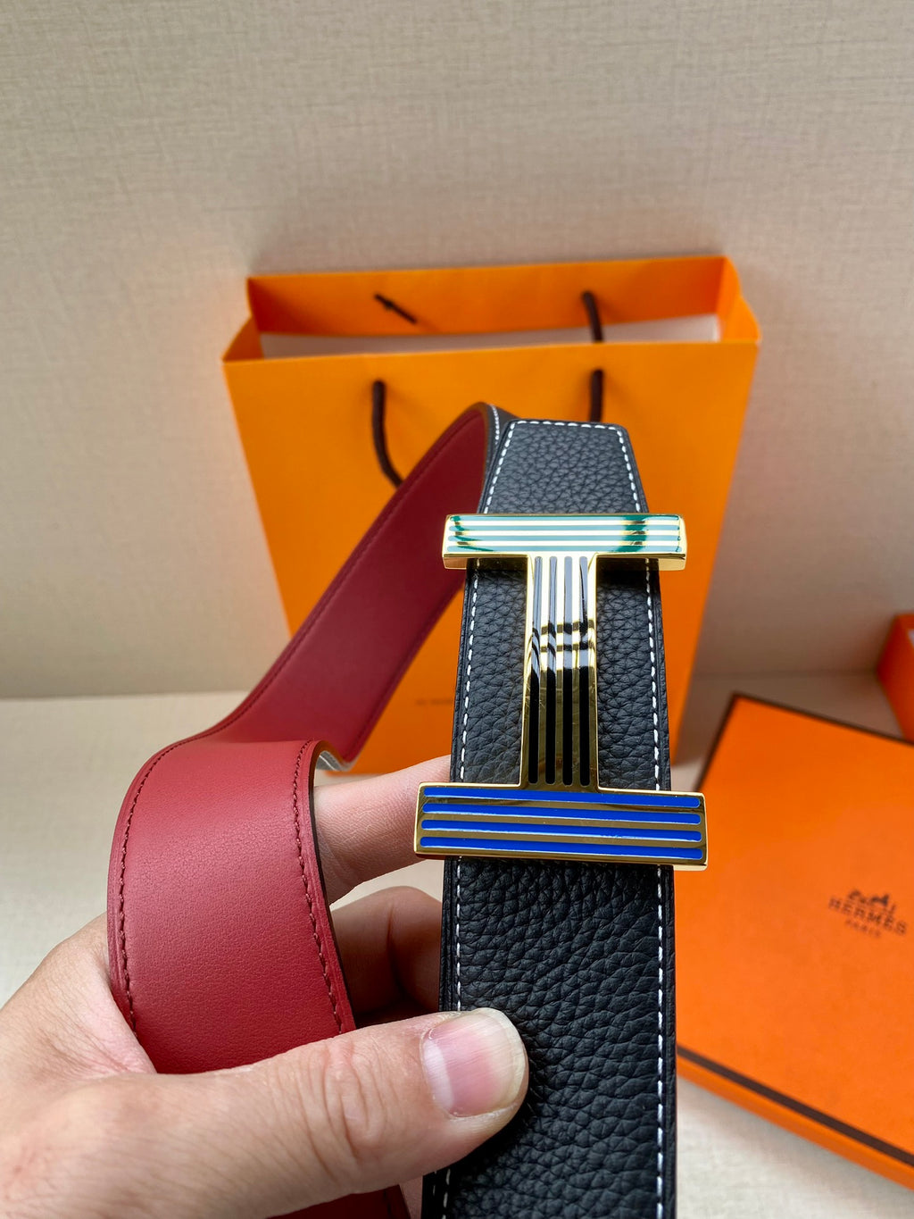 Hermes belt shown close-up with dark blue leather strap and striped rectangular buckle
