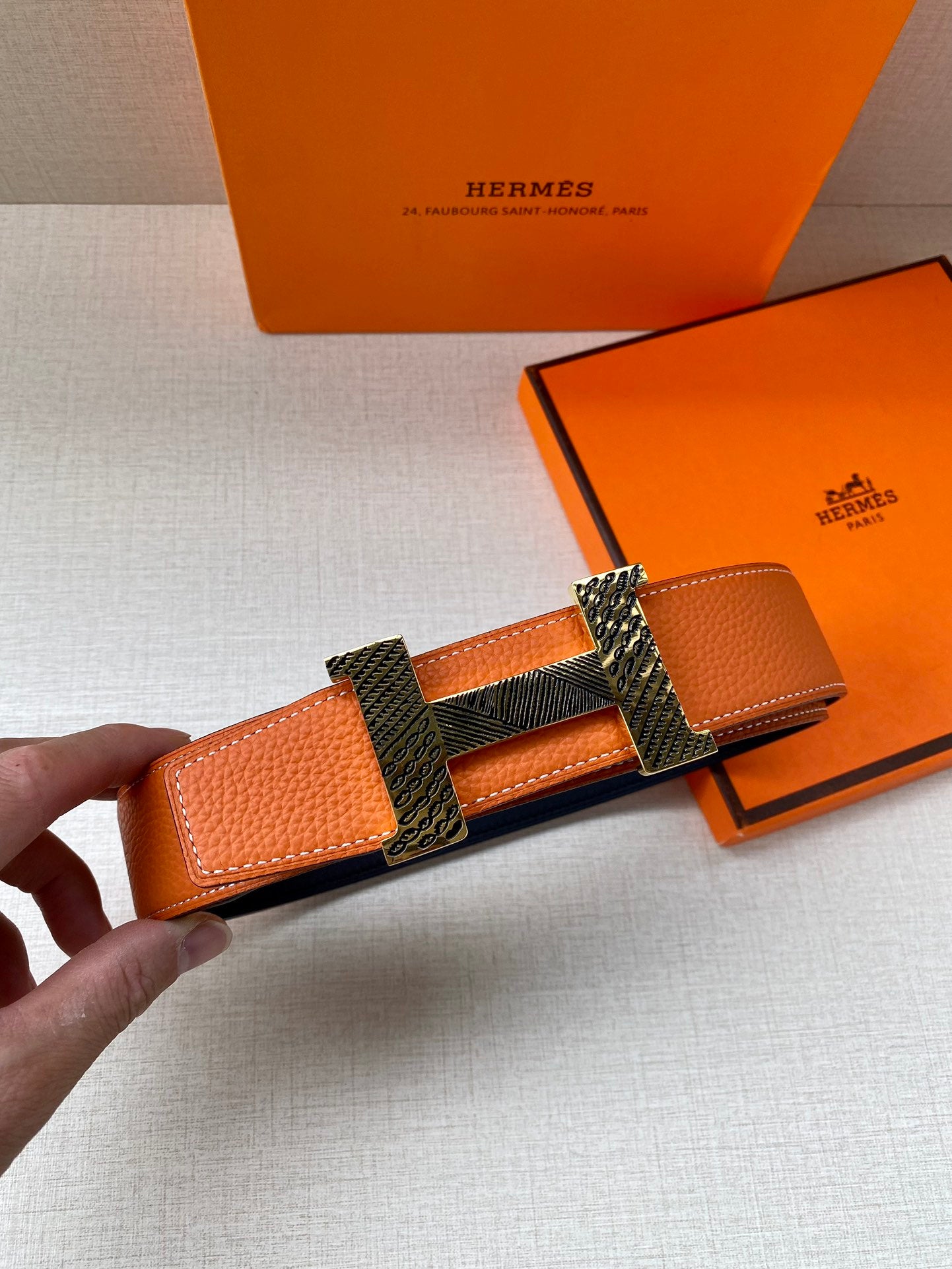 Orange leather belt with textured strap and gold-tone H buckle detail, held up