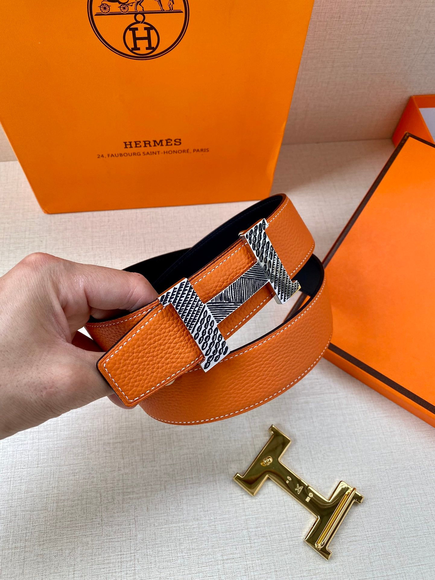 Orange textured leather belt with navy underside and gold-tone H buckle detail