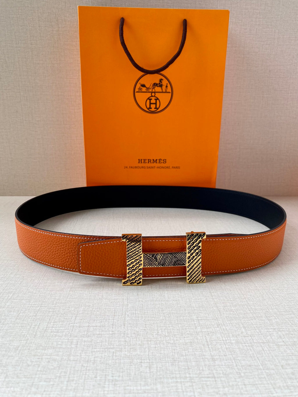 Orange leather belt with navy interior and gold-tone buckle, laid flat