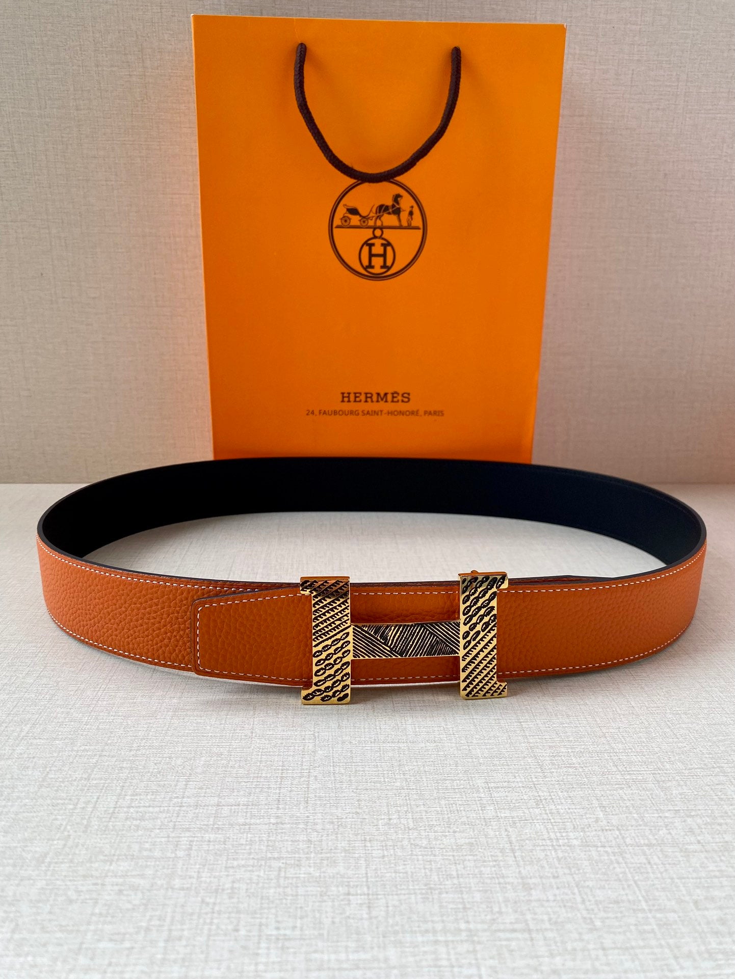 Orange leather belt with navy interior and gold-tone buckle, laid flat