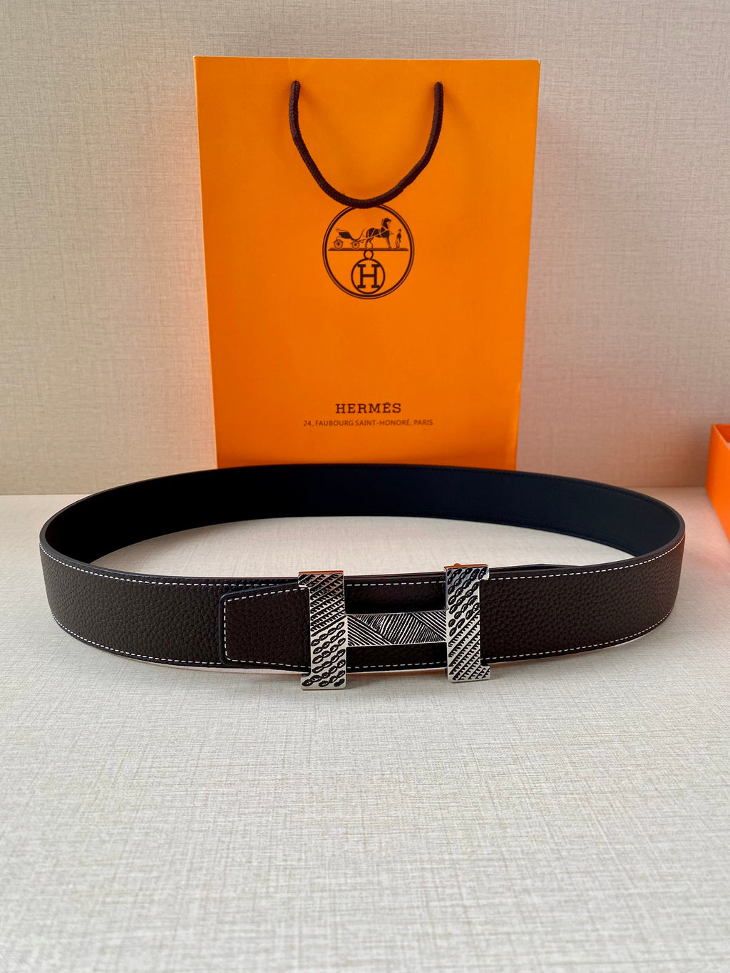Hermes belt laid flat, black textured leather with gold-tone and silver buckle