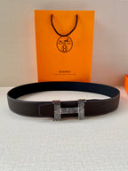 Hermes belt laid flat, black textured leather with gold-tone and silver buckle