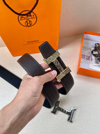 Hermes belt held at an angle, black textured leather with gold-tone buckle