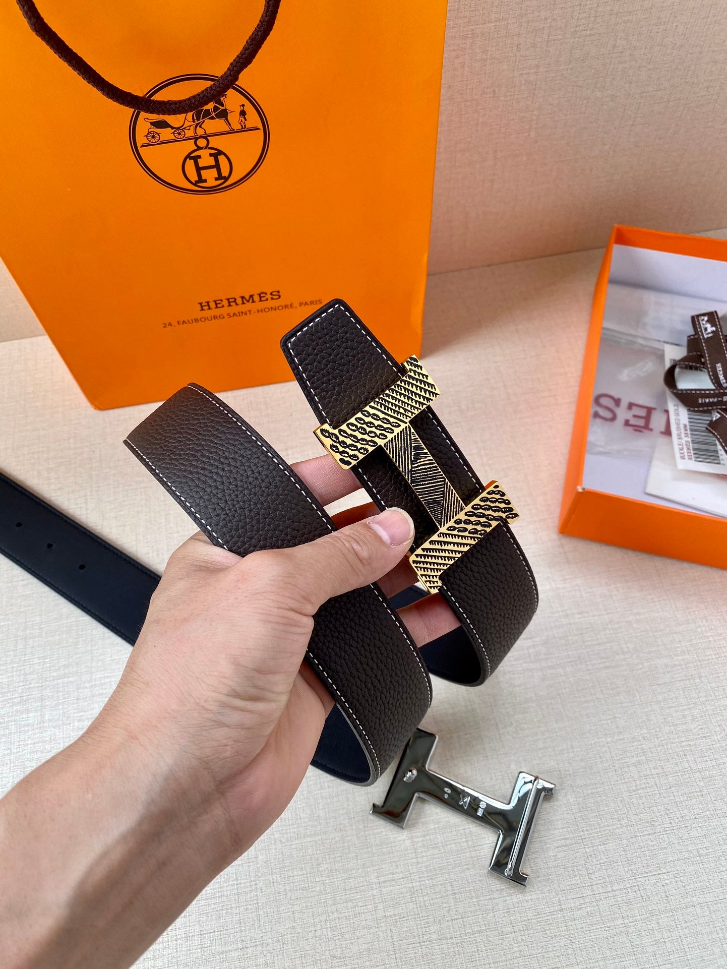 Hermes belt held at an angle, black textured leather with gold-tone buckle