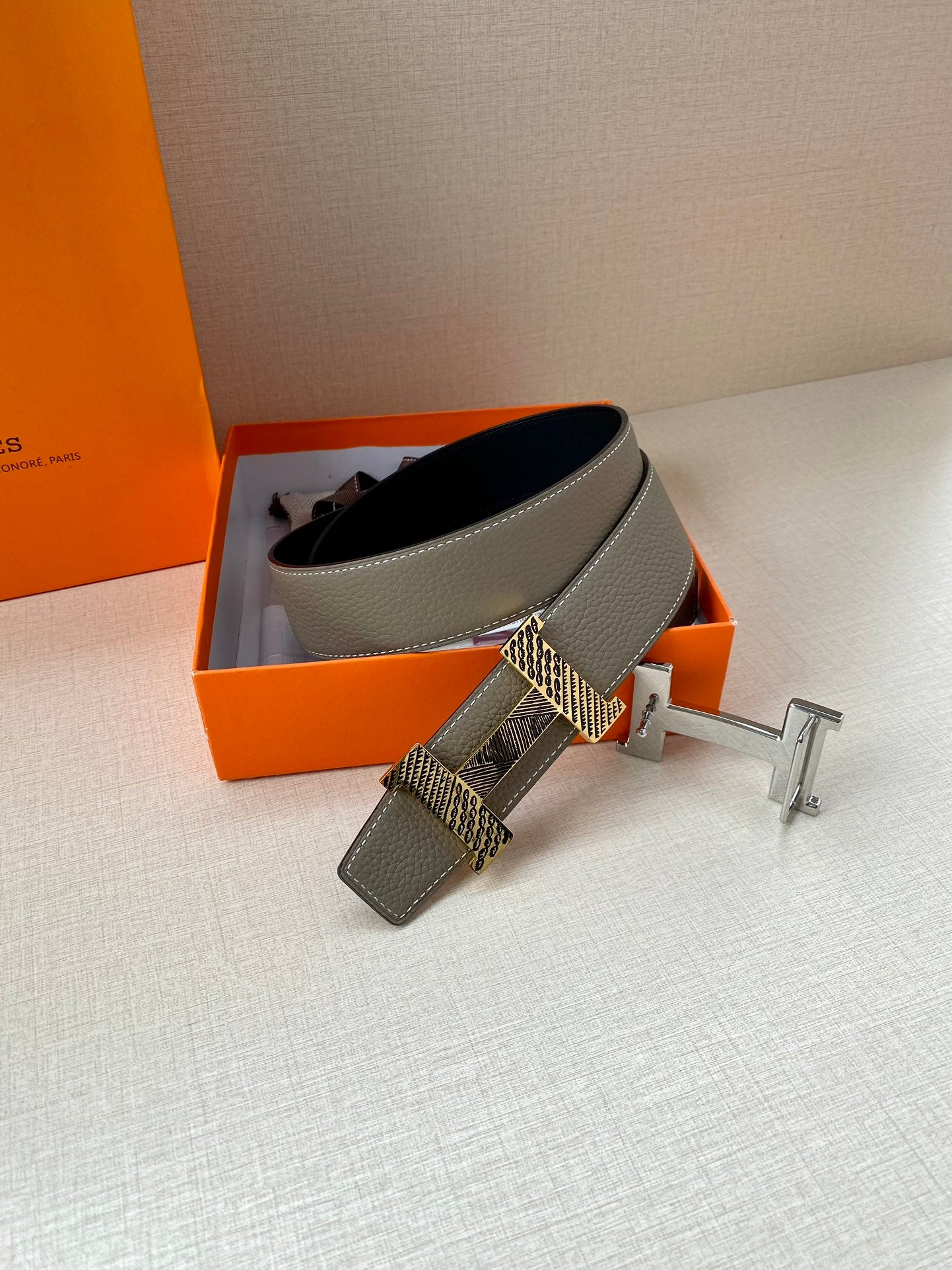 Hermes belt with gray leather band and dark underside, gold H buckle on stand