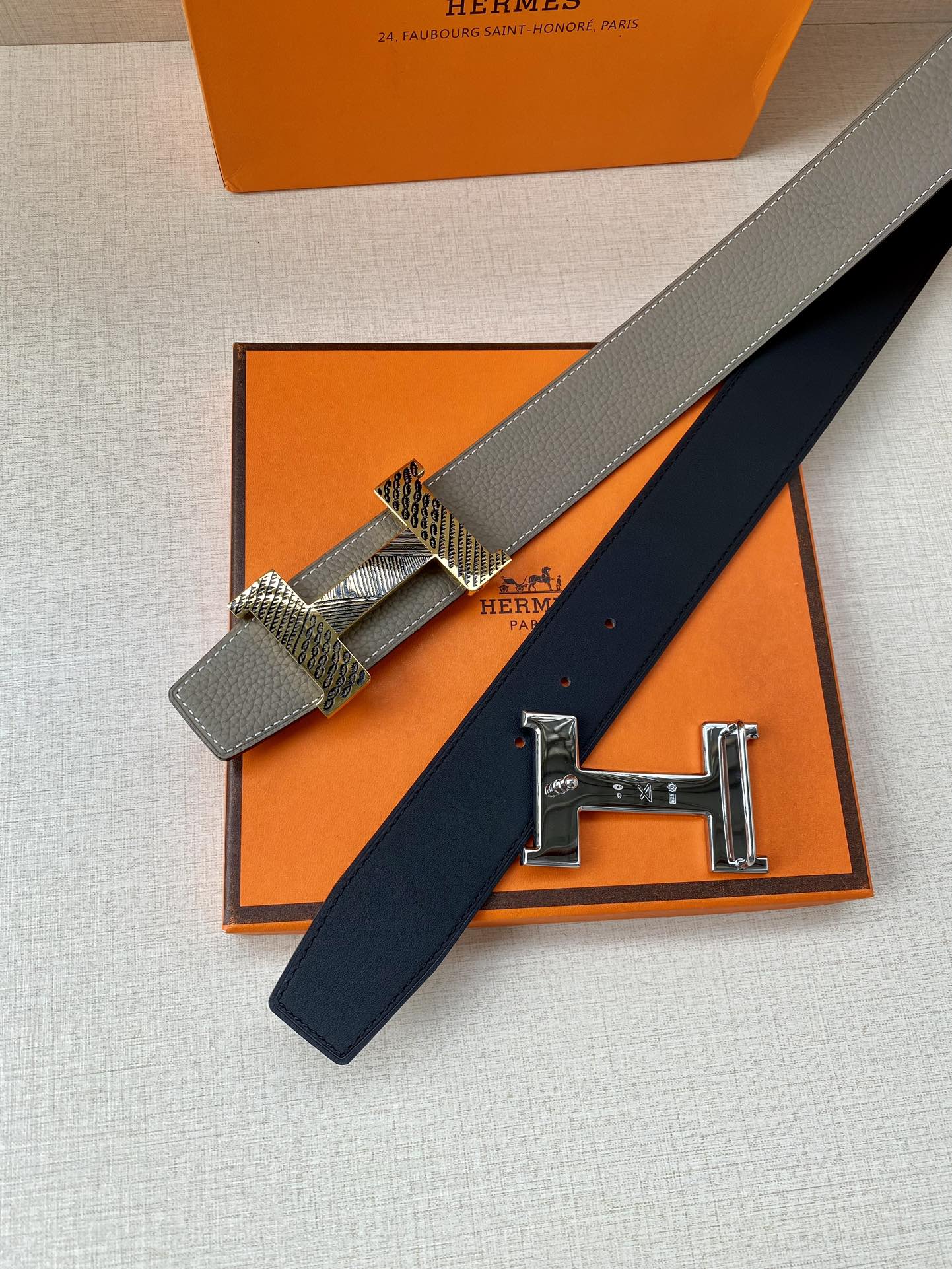 Hermes belt detail showing gray strap, woven keeper, and gold H hardware over box