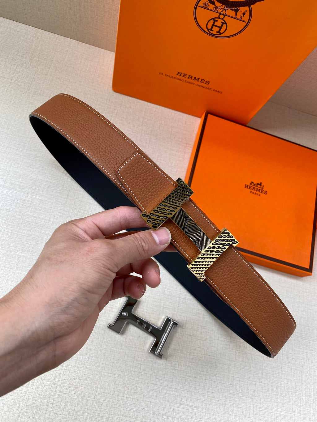 Hermes leather belt with brown strap and silver-tone buckle, held in hand