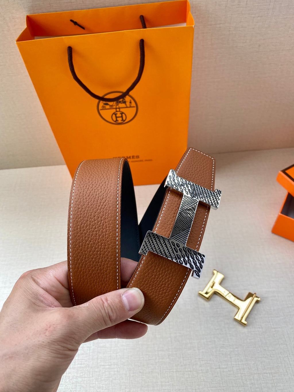 Hermes leather belt with brown strap and textured silver-tone buckle, shown by hand