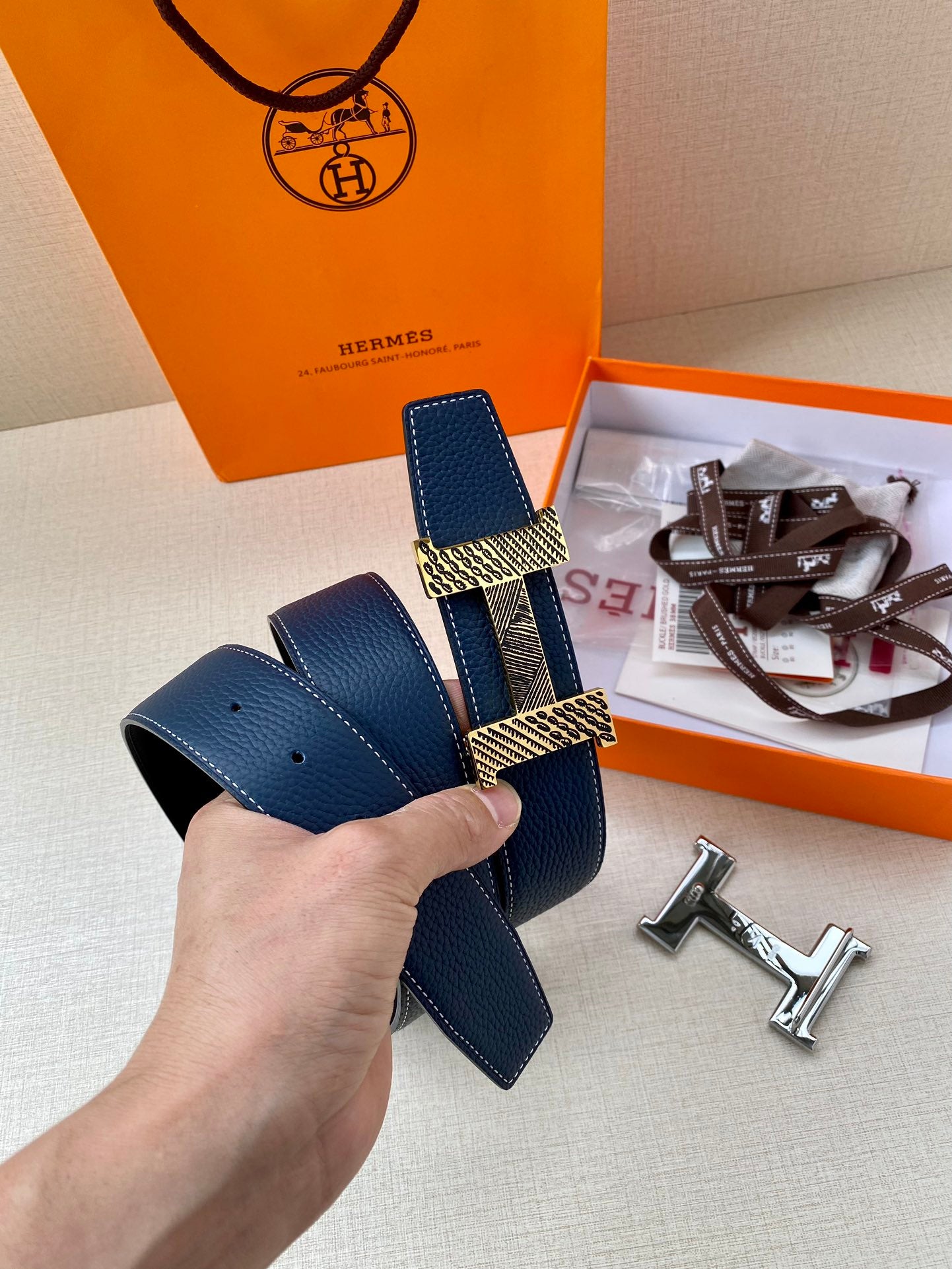 Blue leather belt with gold-tone buckle plates, silver buckle hardware, hand holding