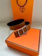 Hermes belt with tan strap and silver-tone triple square buckle resting on box