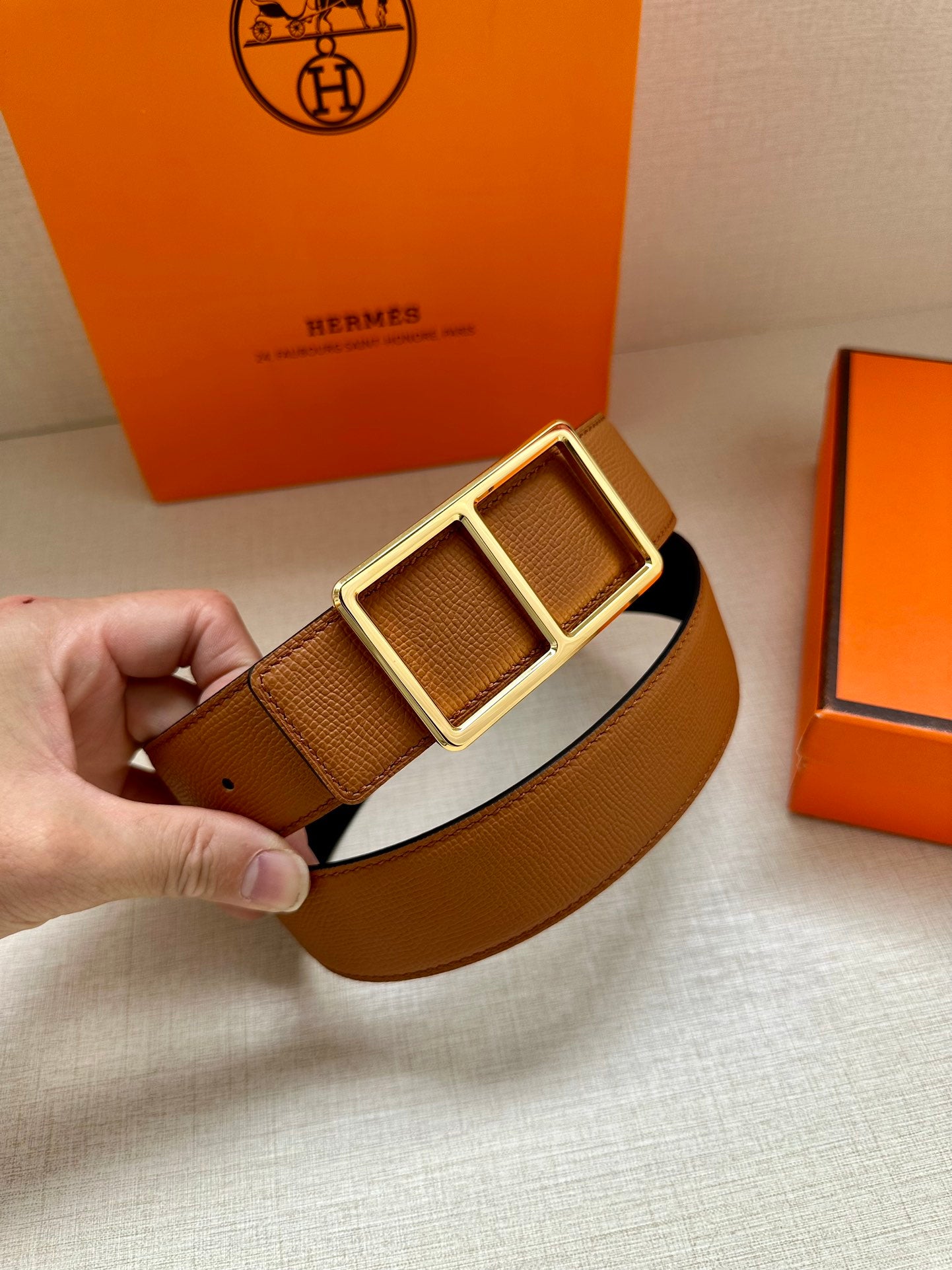 Hermes belt close-up: tan textured strap with gold-tone double square buckle