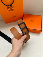 Hermes belt with tan leather strap and square buckle detail, held in hand