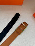 Hermes belt laid flat: tan strap with gold-tone square buckle next to black strap