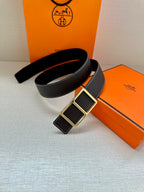 Leather belt with textured dark strap and gold-tone square buckle, coiled on box