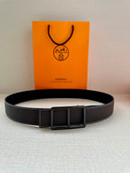 Leather belt with smooth dark strap and rectangular buckle, centered on surface