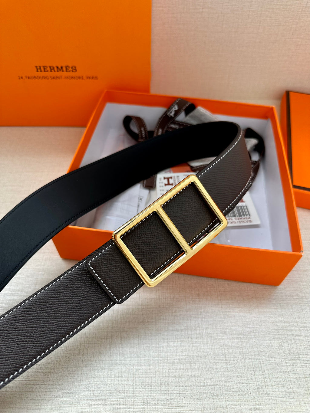 Leather belt with textured dark strap and gold-tone square buckle, laid across box