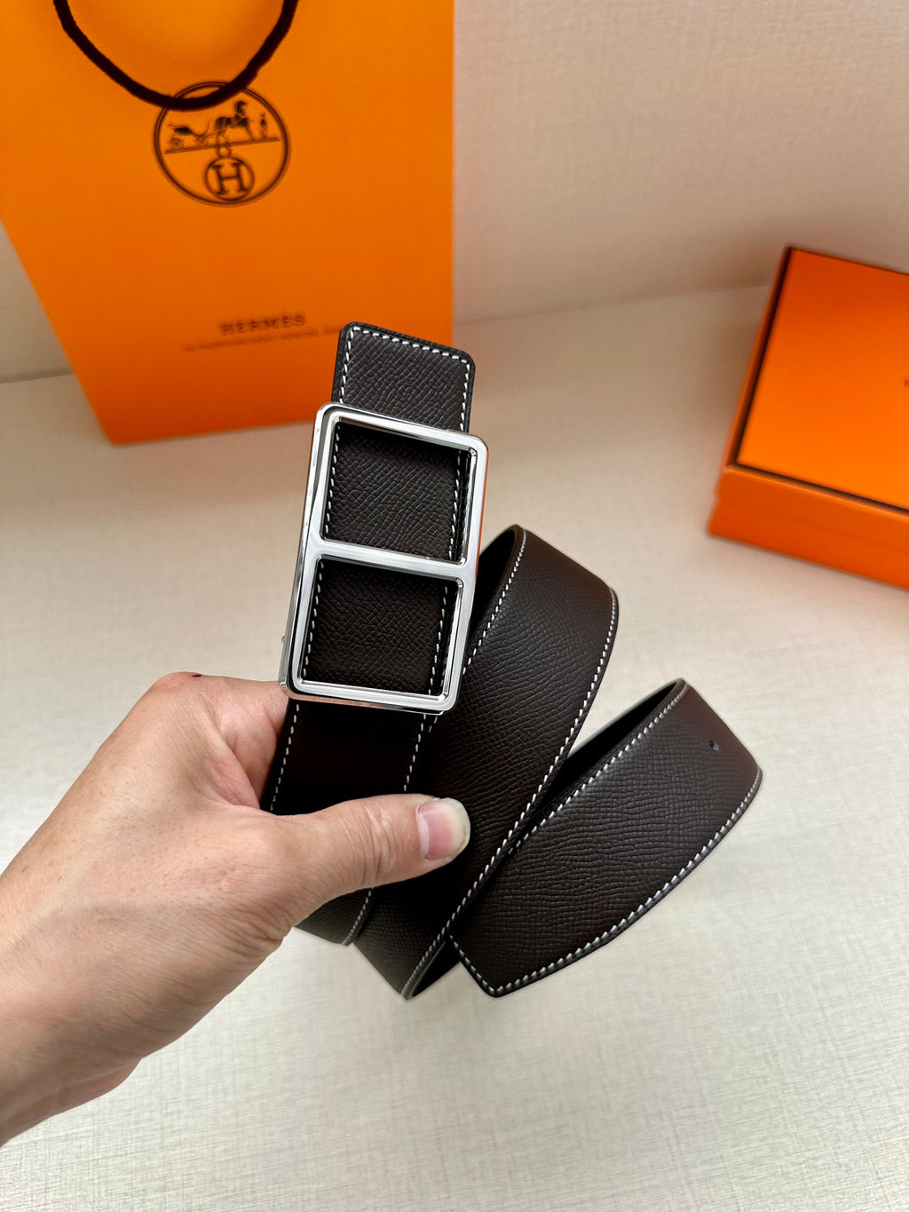 Leather belt with textured dark strap and silver-tone buckle, close-up held by hand