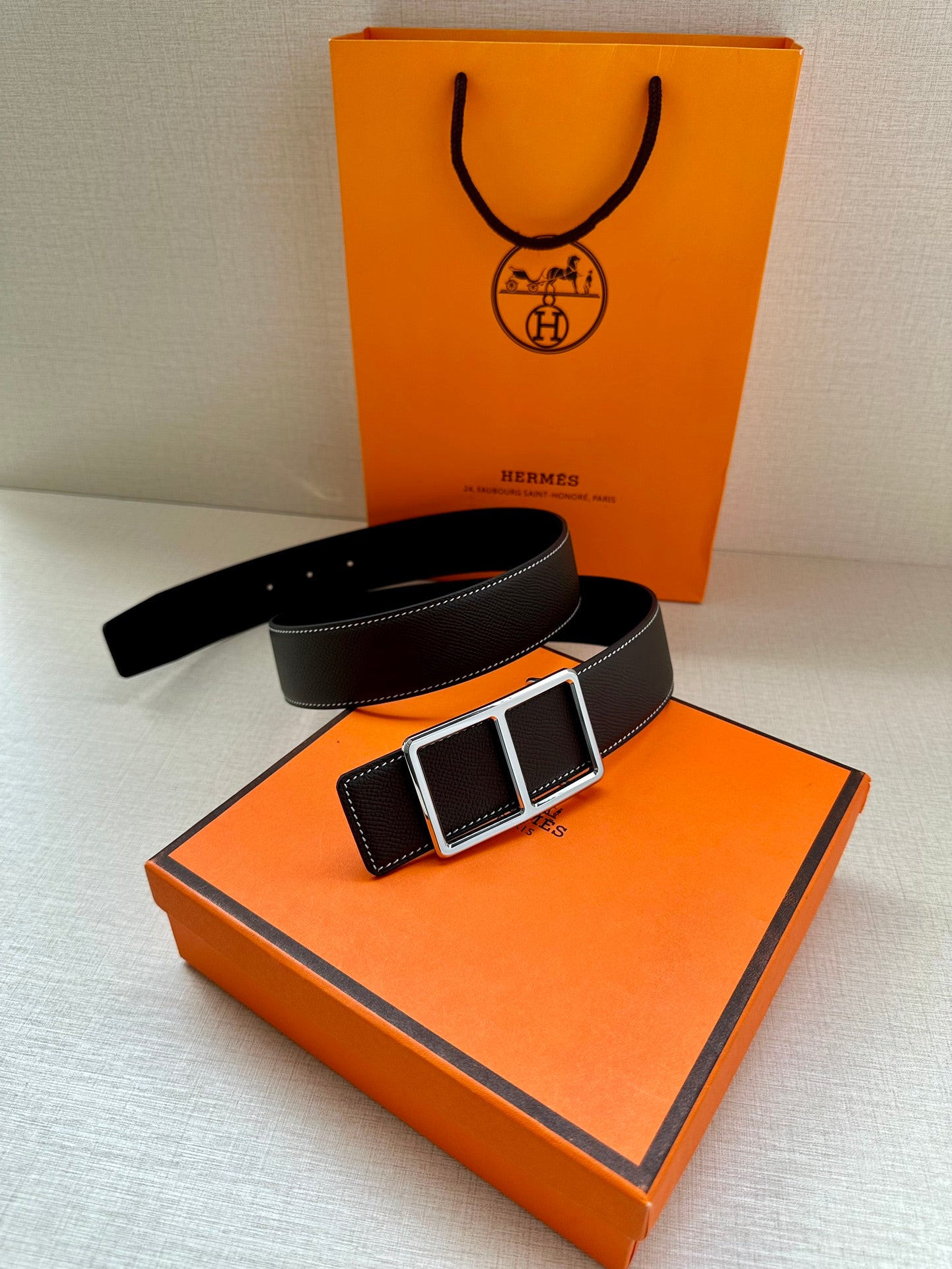 Leather belt with textured dark strap and silver-and-black buckle on an orange box