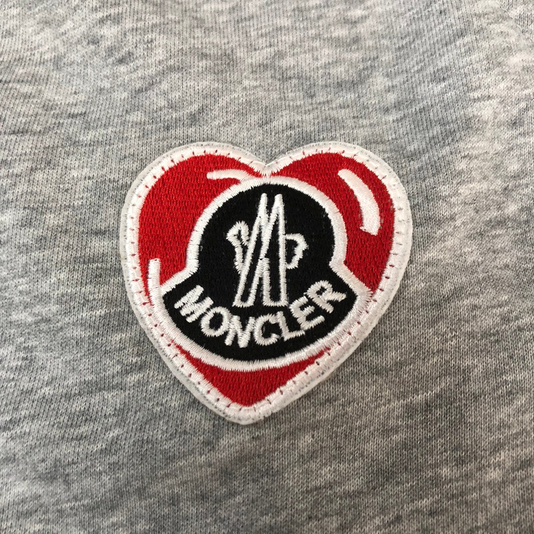 Heart-shaped Moncler logo patch on gray shorts fabric.