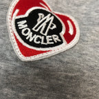 Heart-shaped Moncler logo patch on gray fabric with red and black details.