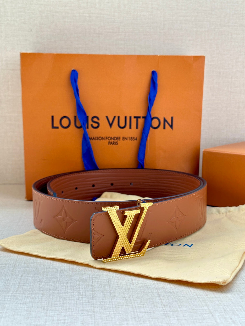Louis Vuitton belt with brown embossed strap and gold-tone LV buckle in front of box