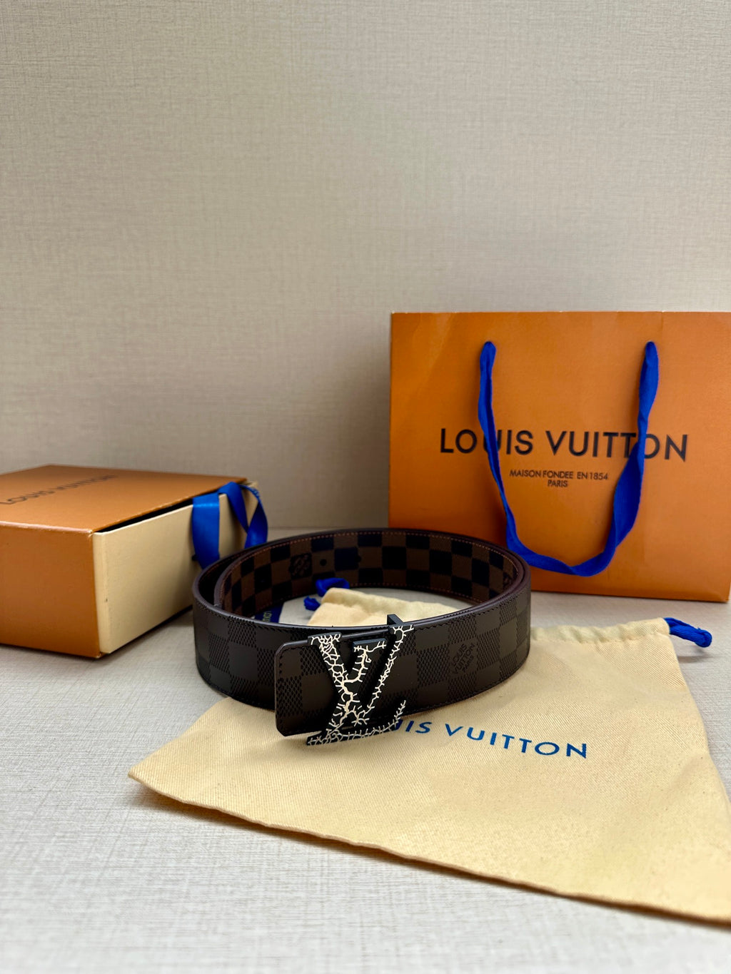 Louis Vuitton belt with dark checker strap and metallic LV buckle, on fabric cover