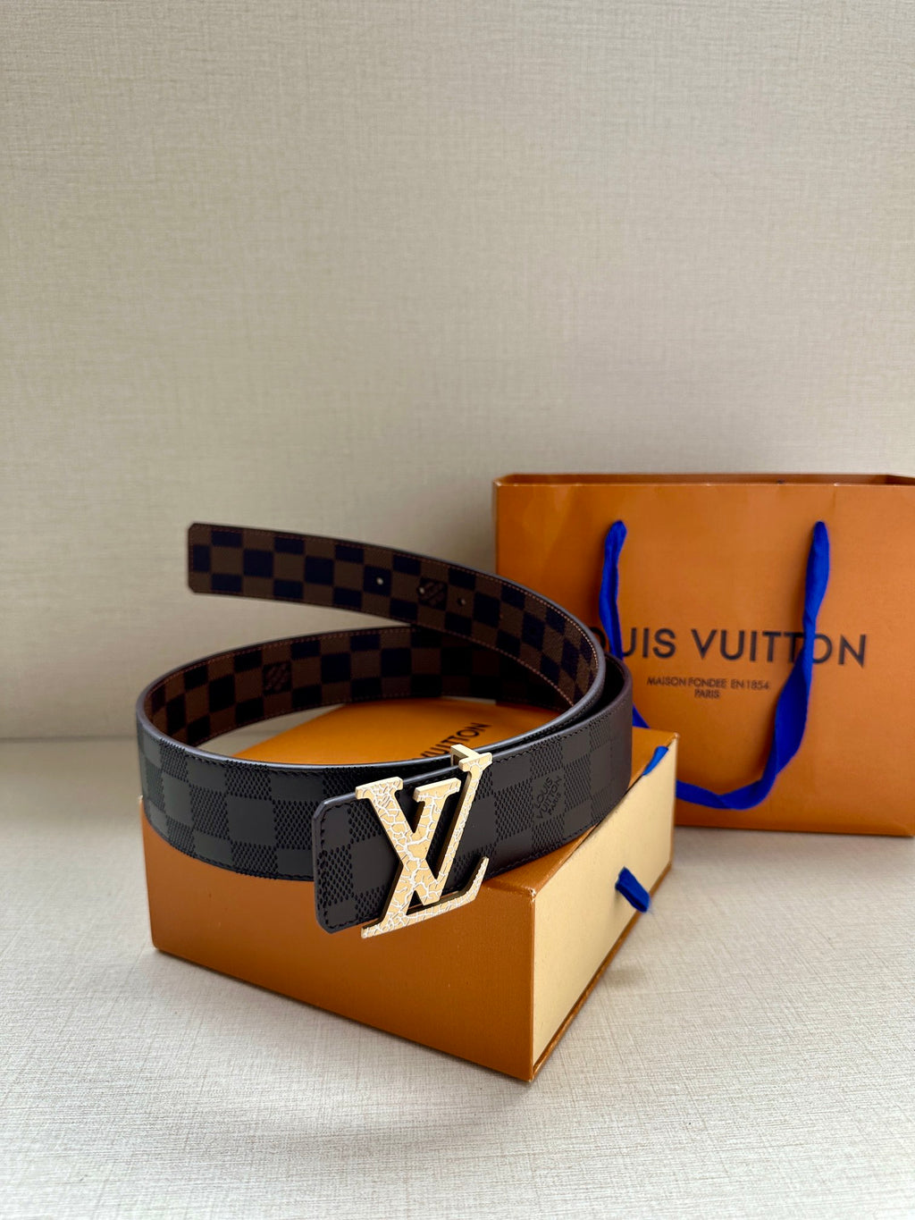Louis Vuitton belt with dark checker strap and metallic LV buckle, angled view
