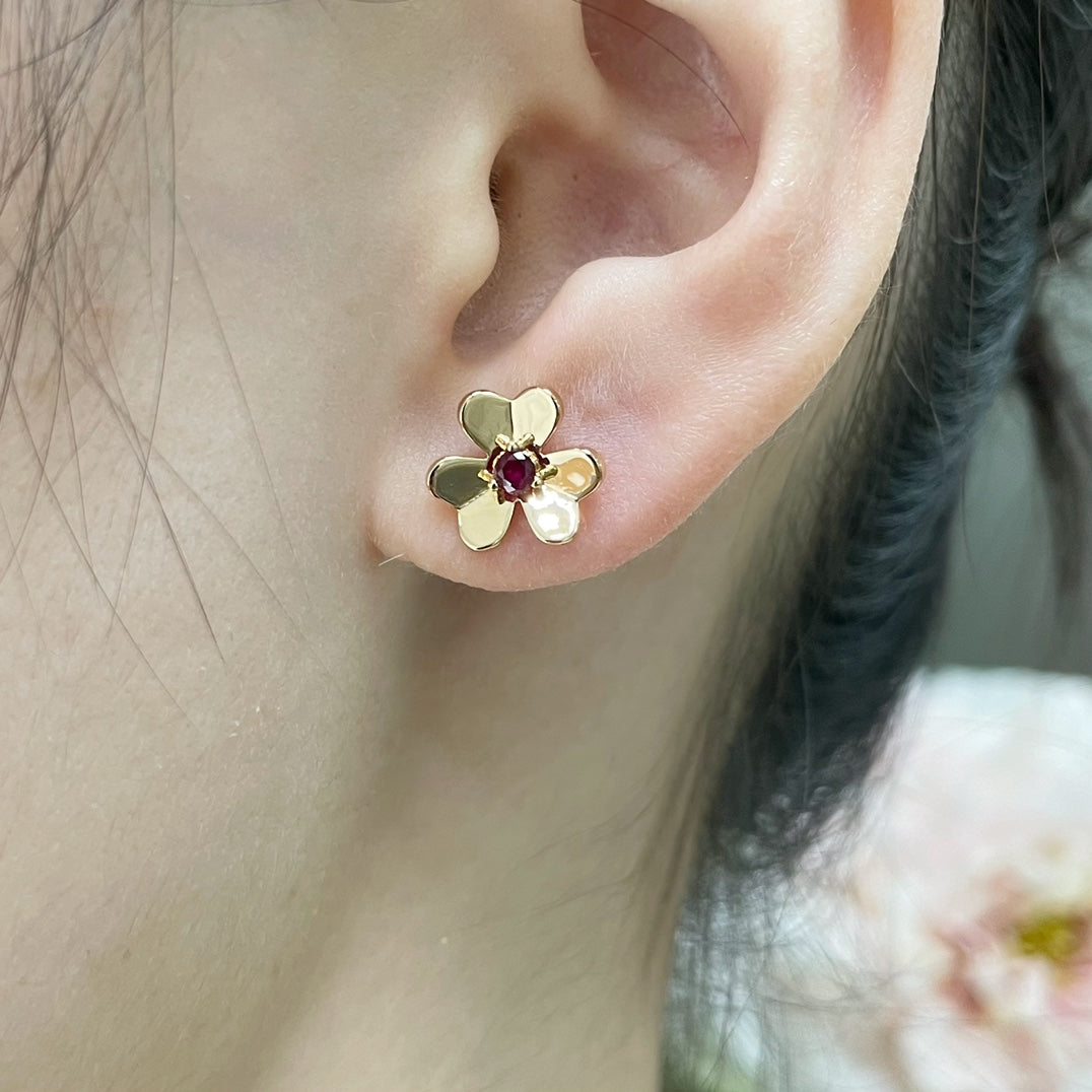 Gold-tone floral stud earring with ruby red center stone on ear