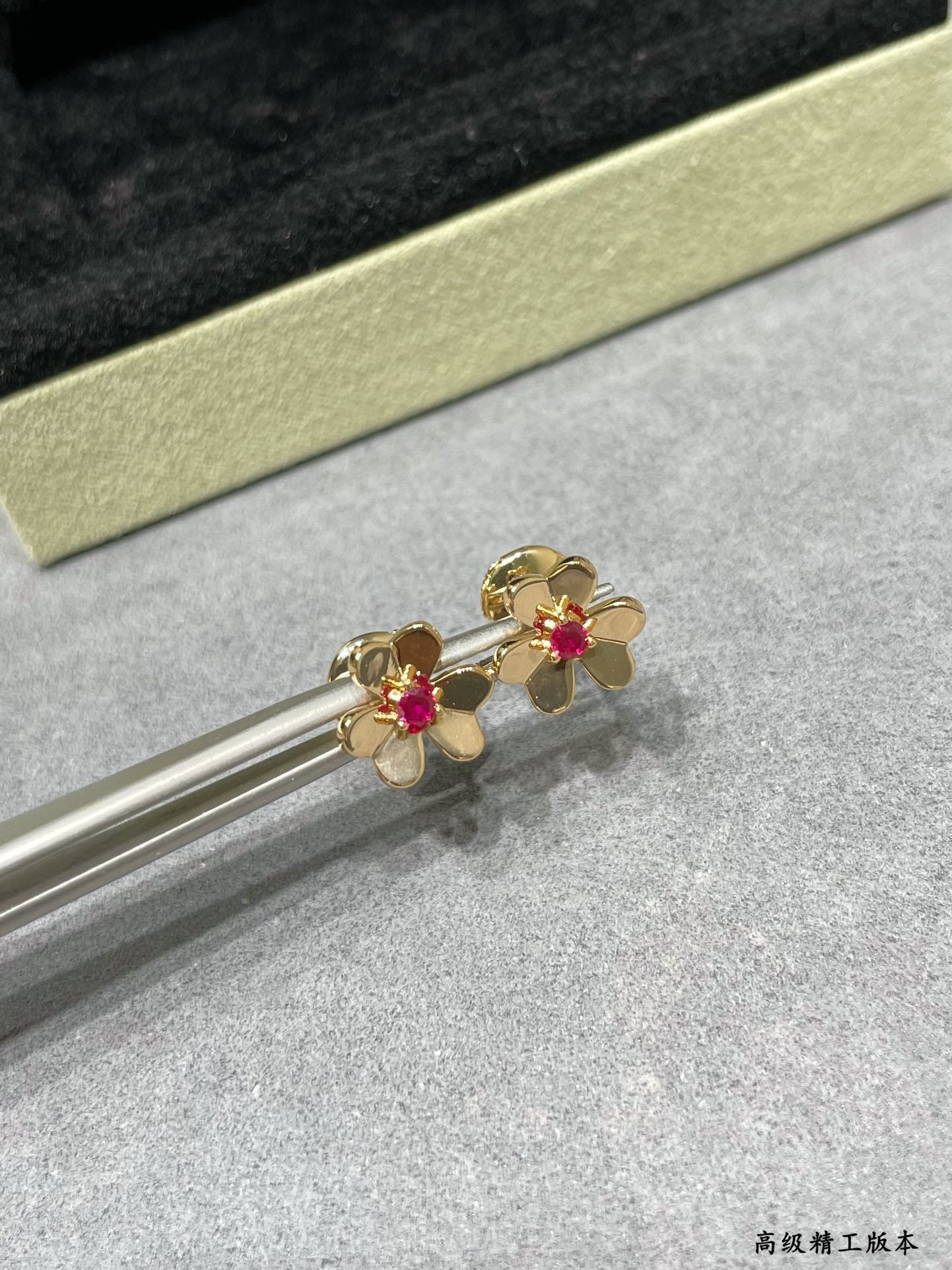 Gold-tone floral stud earrings with ruby red center stones on jewelry tray