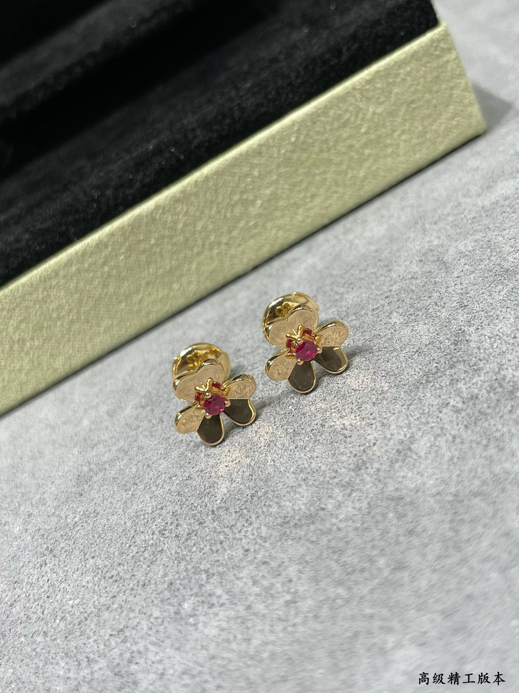 Gold-tone floral stud earrings with ruby red center stones on jewelry stand