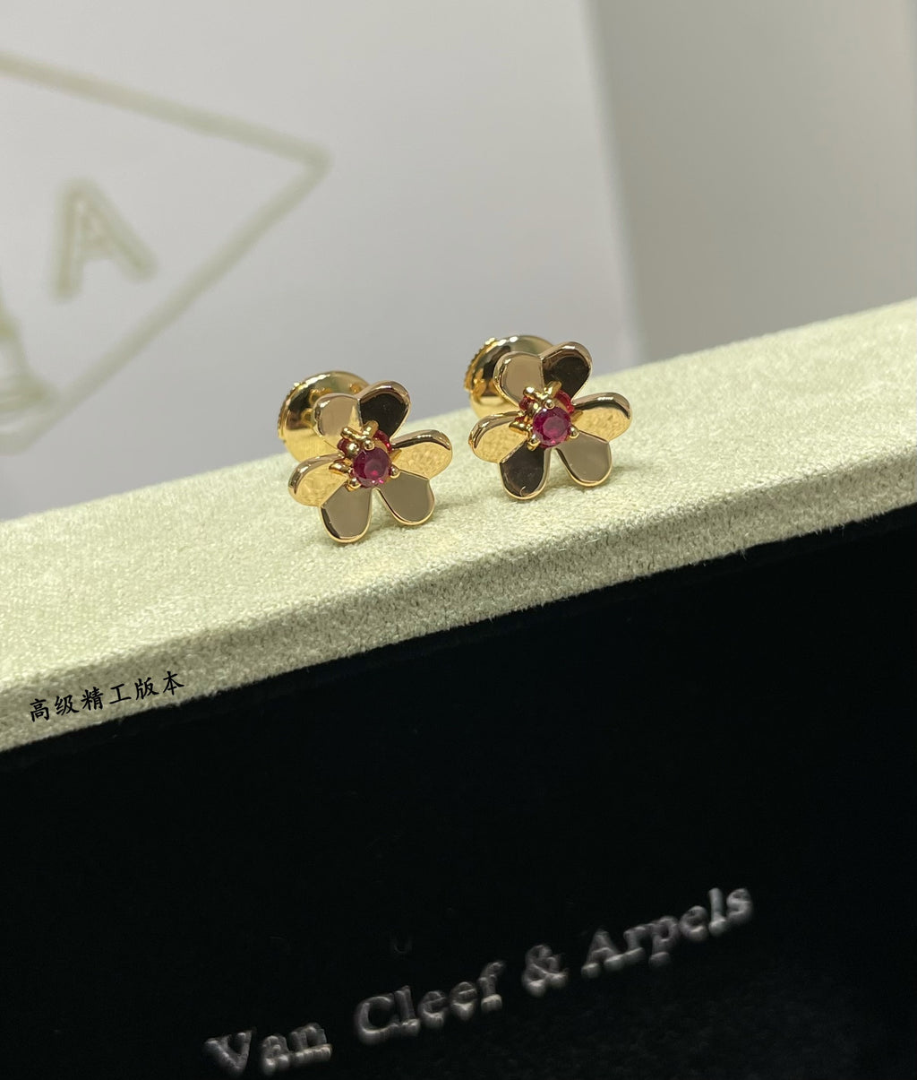 Gold-tone floral stud earrings with ruby red center stones, shown on display box