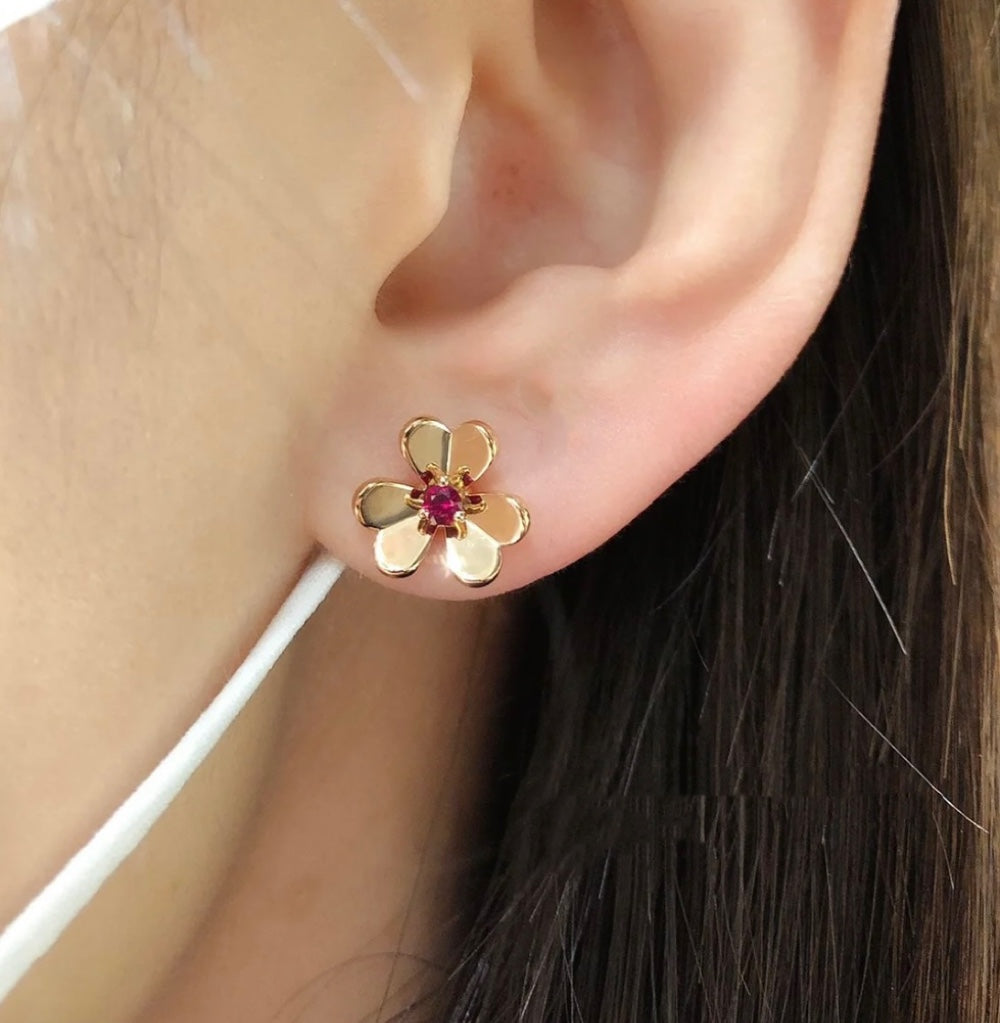 Gold-tone floral stud earring with ruby red center stone on ear