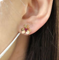 Gold-tone floral stud earring with ruby red center stone on ear