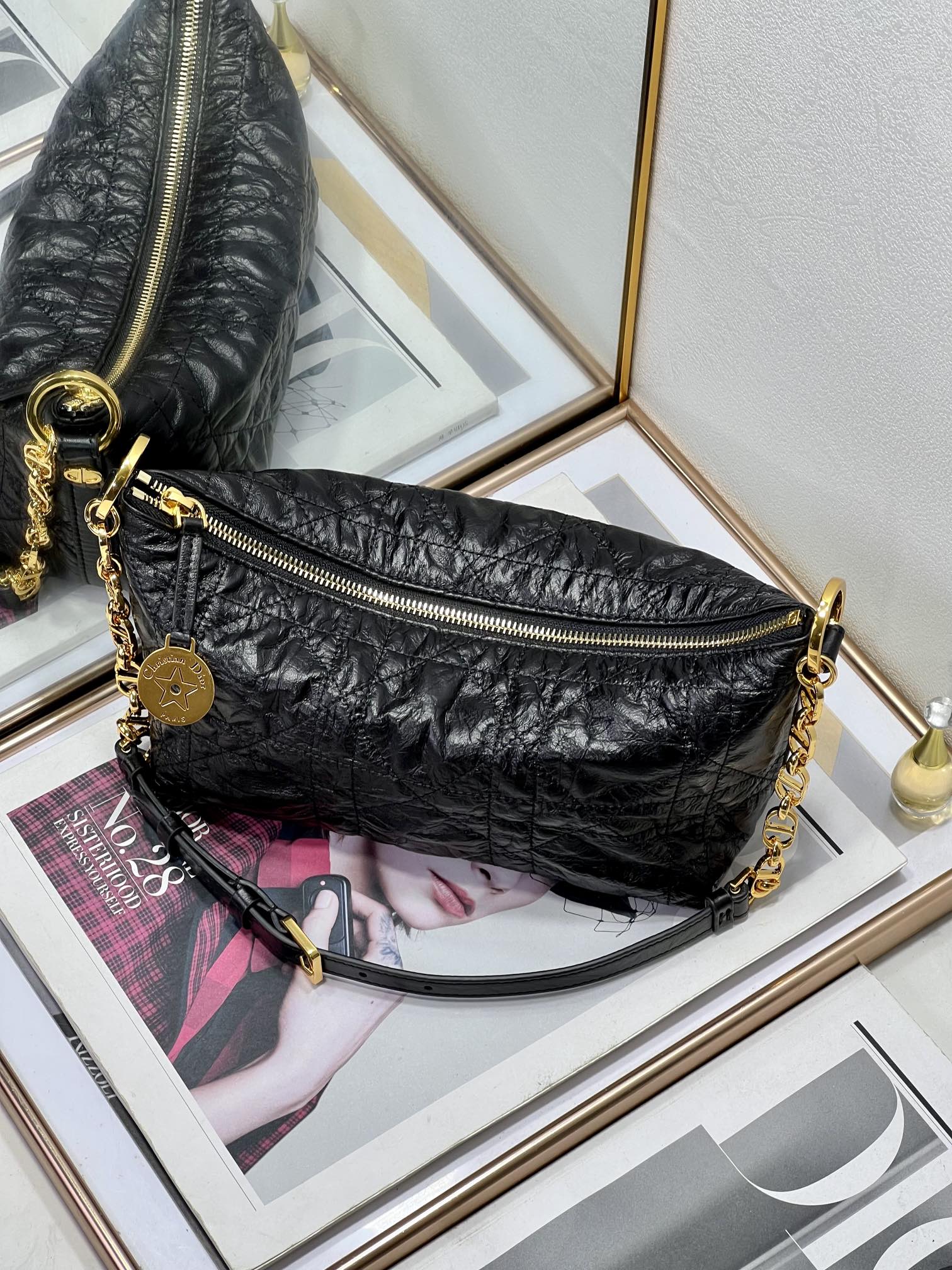 Dior black hobo bag with gold zipper, chain strap, and round logo charm.