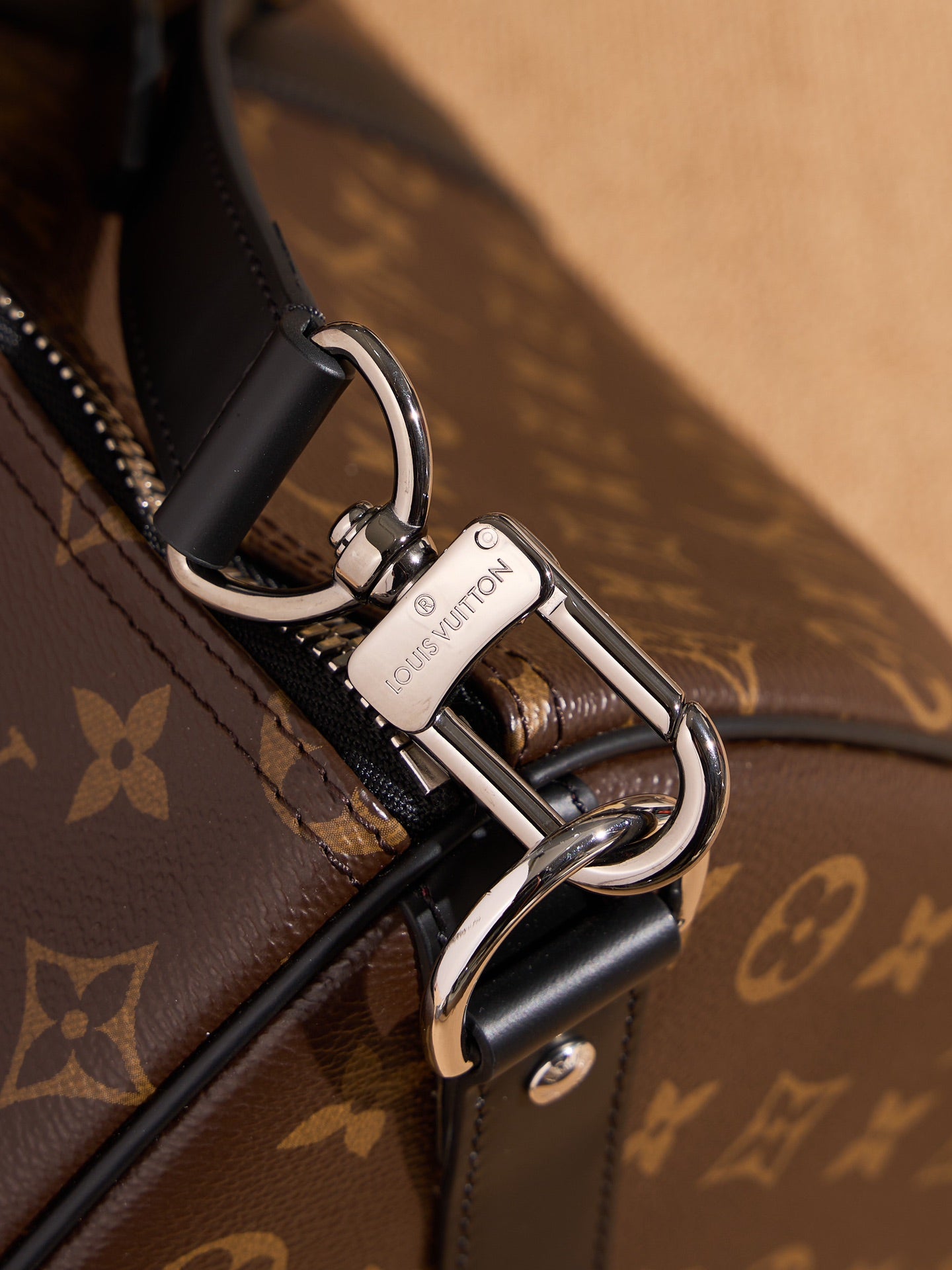Silver-tone clasp and strap attachment on monogram duffel bag, black leather