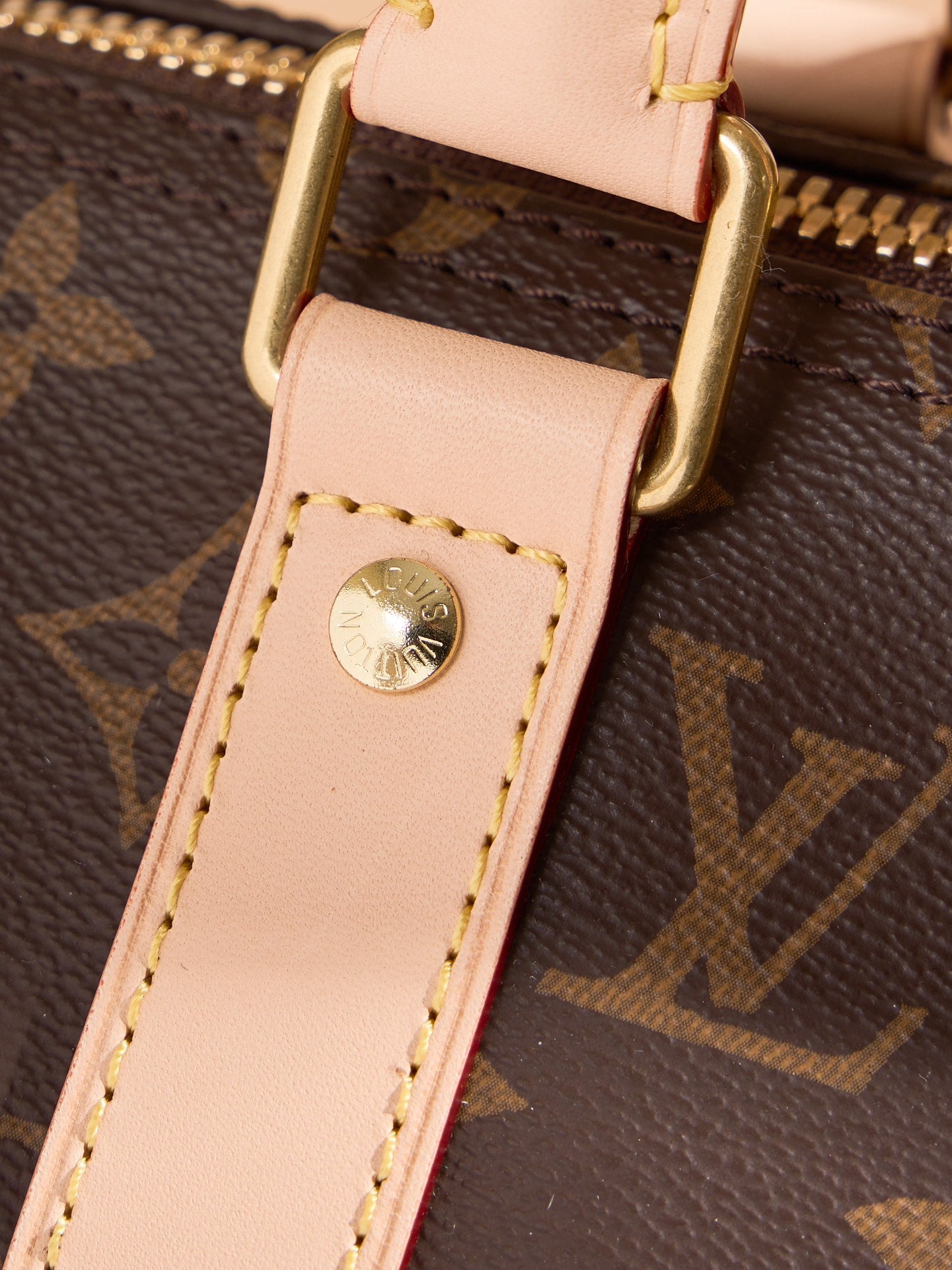 Monogram duffel bag strap end with light tan leather tab and gold logo rivet
