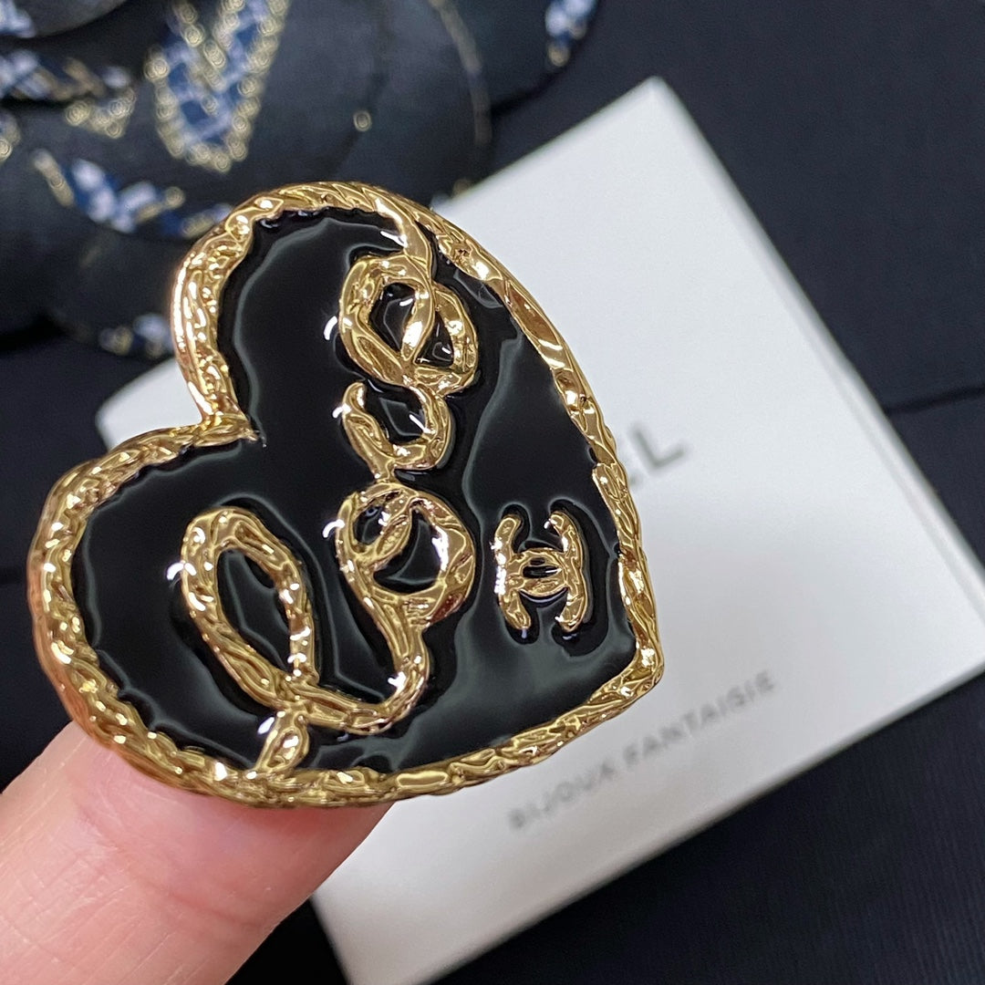 Close-up heart-shaped gold-tone brooch with black enamel front on white Bijoux Fantaisie card