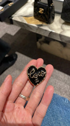 Heart-shaped gold-tone ring with black enamel center on finger
