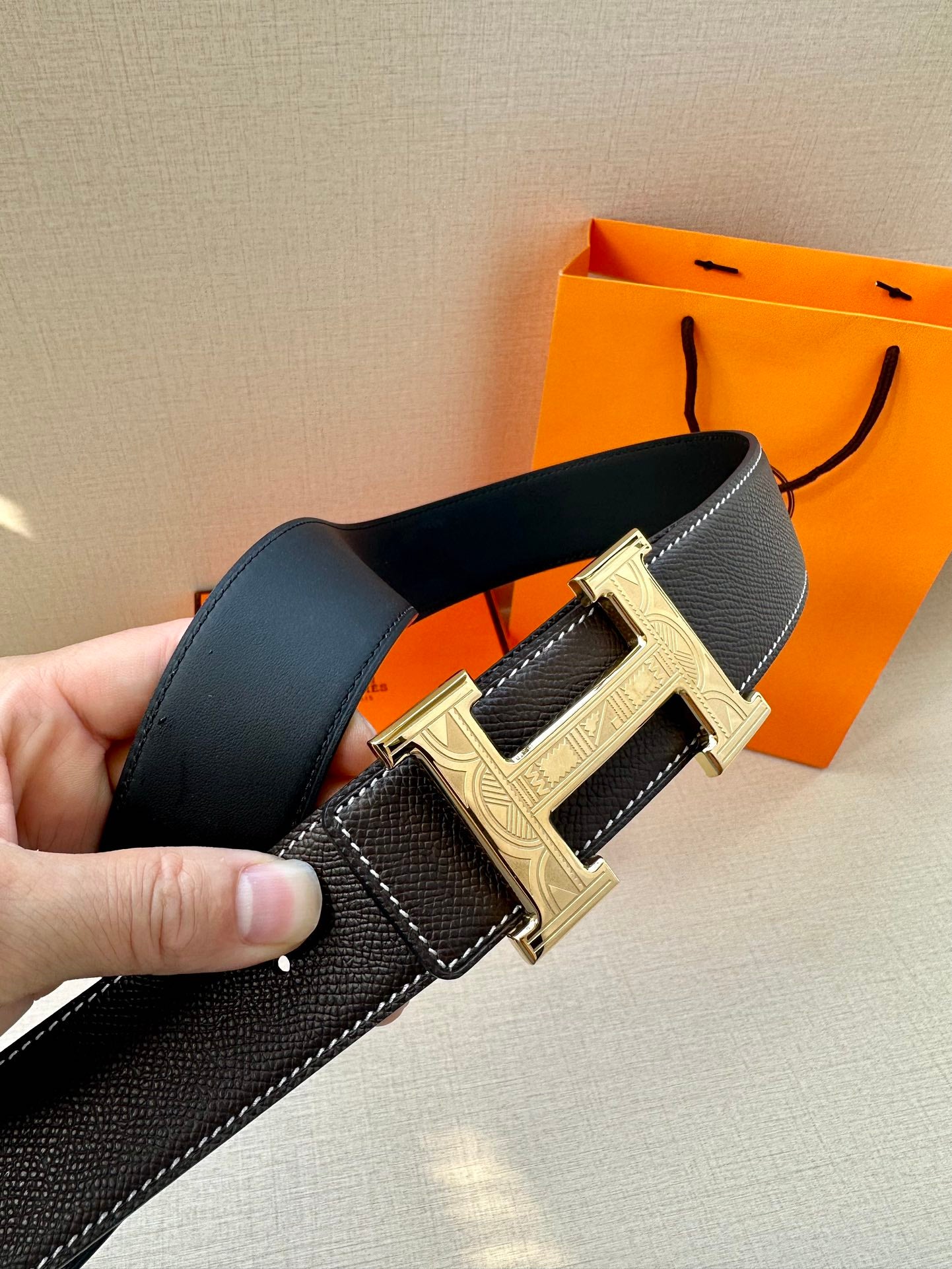 Hermes leather belt with silver double-bar buckle and contrast stitching, held in hand