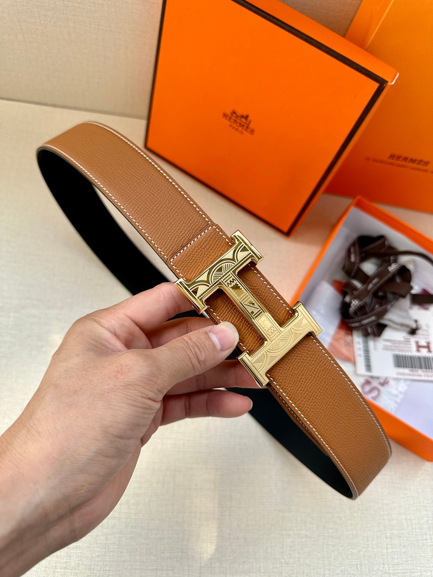 Tan leather belt with metal H buckle, viewed from side in a hand