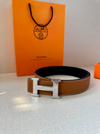 Tan leather belt with metal H buckle and black underside strap, full profile