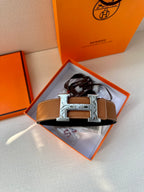 Tan leather belt with metal H buckle displayed in an open box