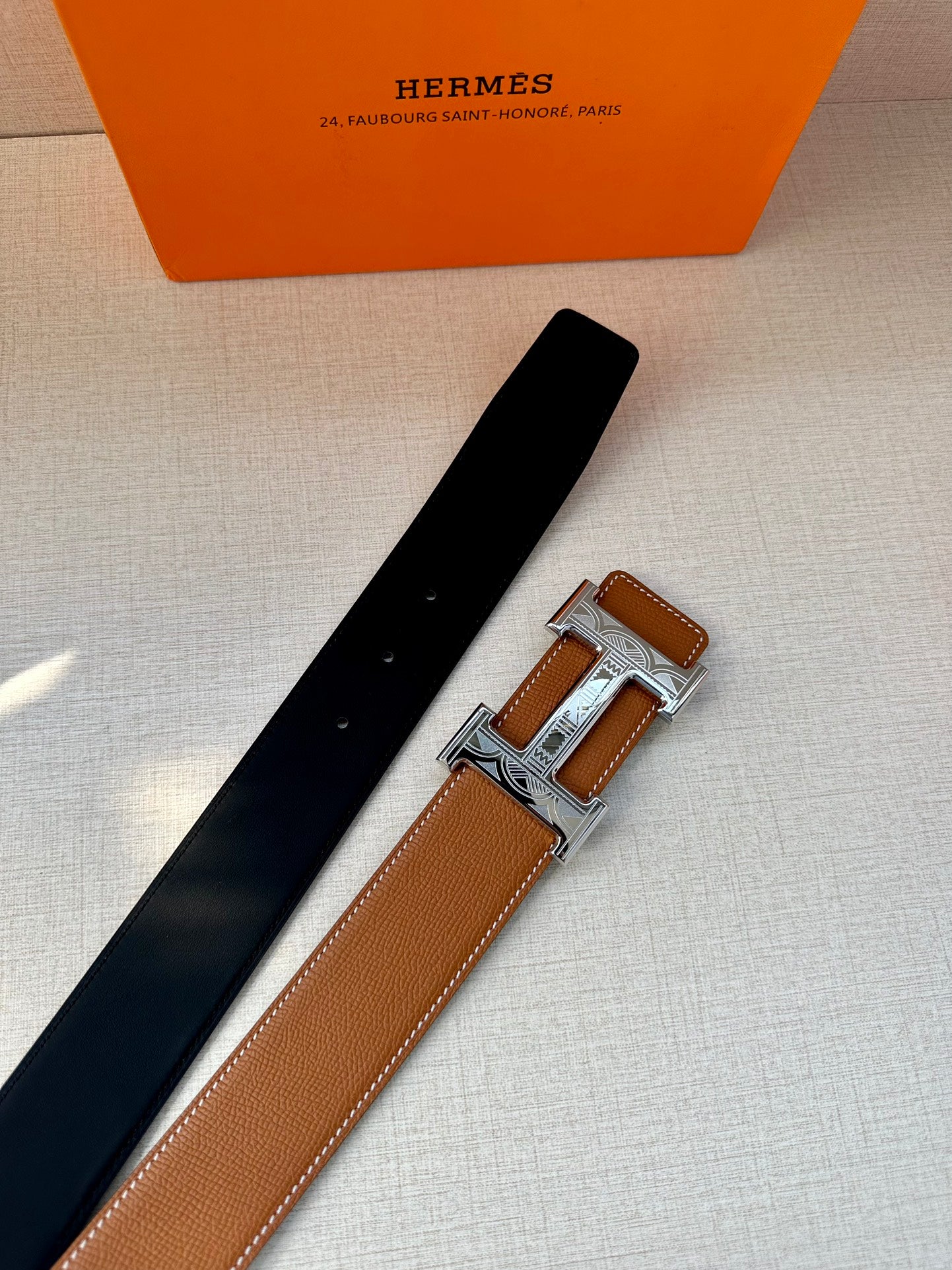 Tan leather belt with metal H buckle, laid flat with dark strap side