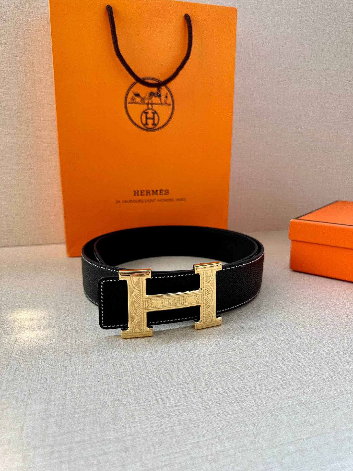 Hermes leather belt on surface, dark navy strap with silver H buckle at center
