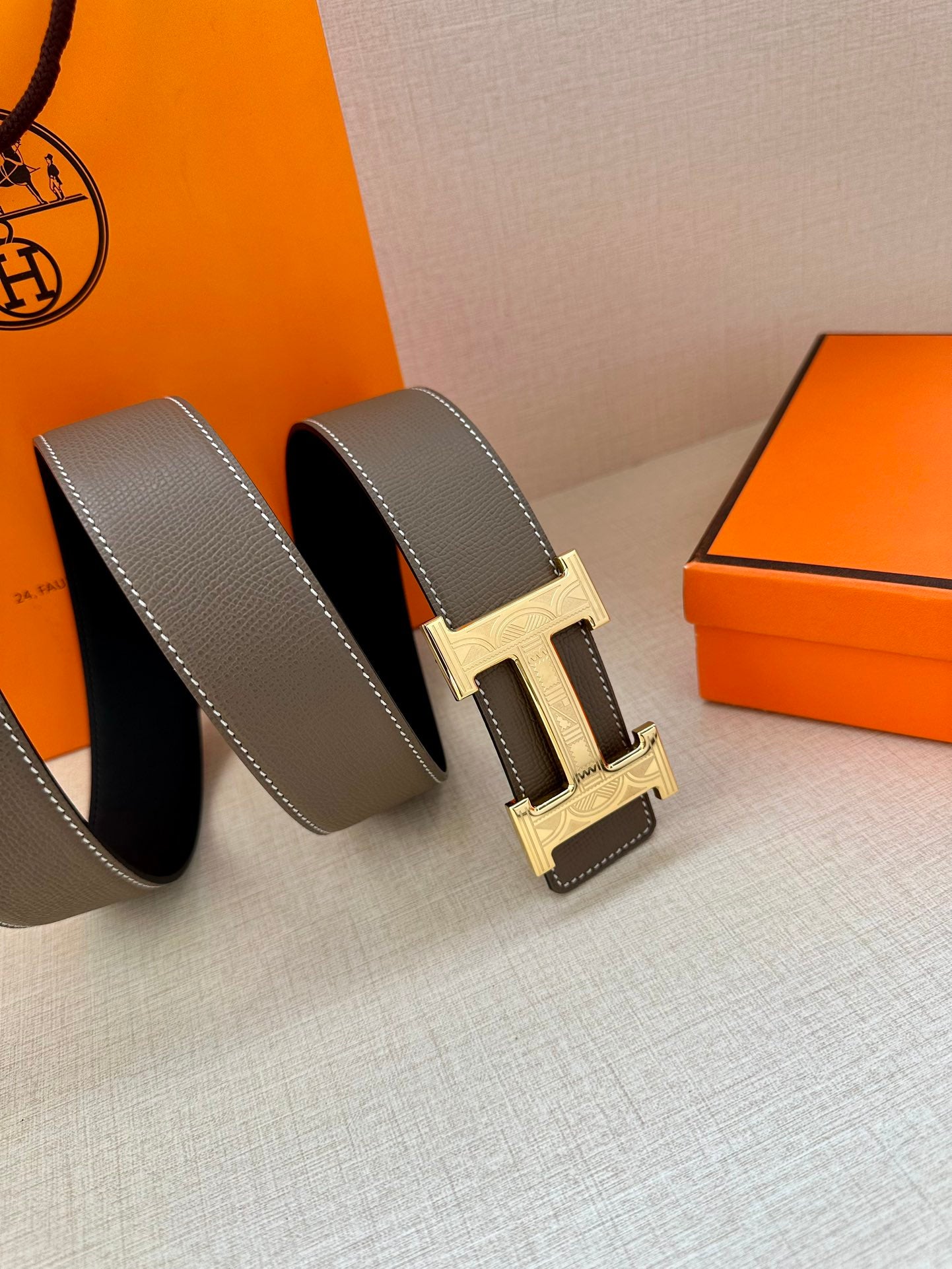 Leather belt with textured gray strap and gold-tone H buckle, stacked side view.